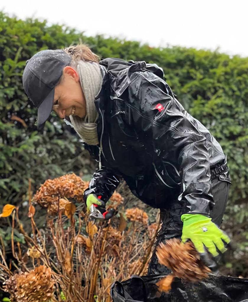 Eine Frau schneidet Sträucher und lächelt, obwohl es regnet.