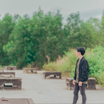 Ein junger Mensch steht auf einer Betonfläche und schaut in Richtung Waldrand.