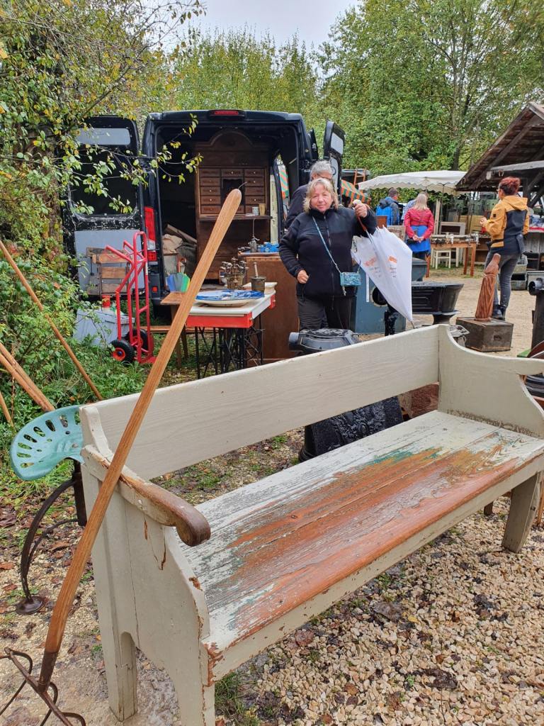 Im Vordergrund ist eine alte Holzbank zu sehen. Dahinter sind Menschen und noch mehr Trödel.