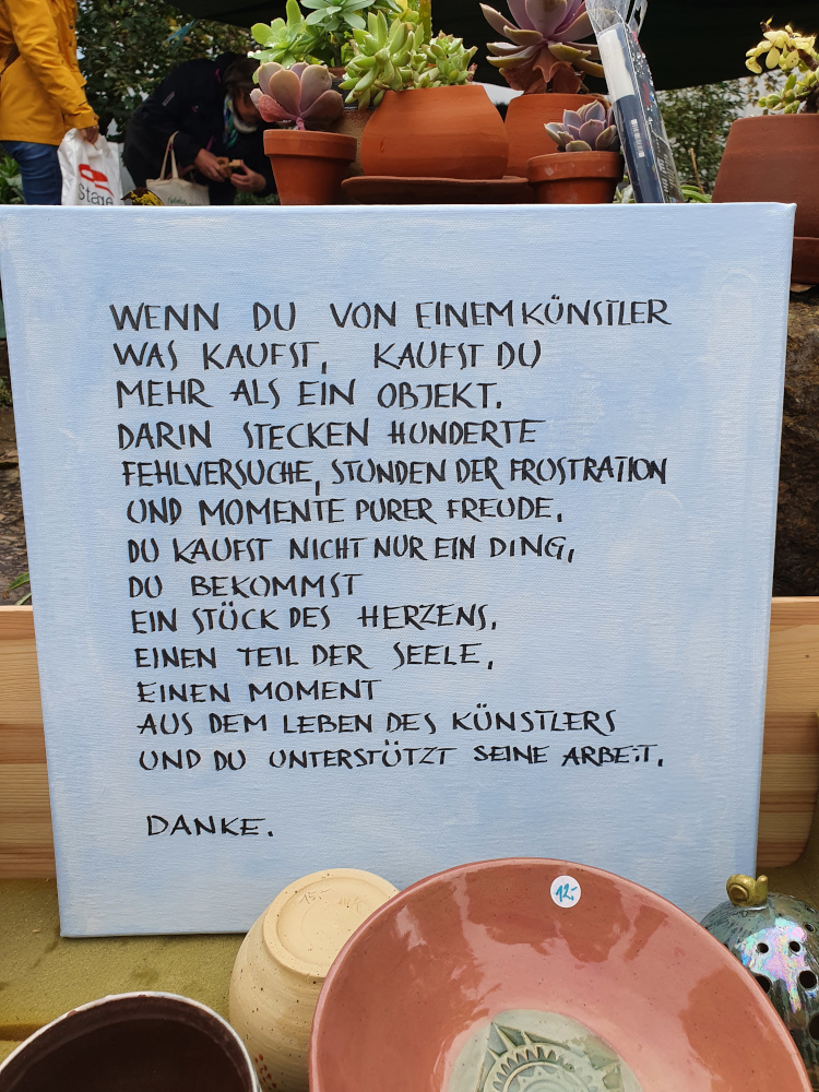 Am Stand einer Künstlerin steht ein Schild: Wenn Du von einem Künstler was kaufst, kaufst Du mehr als nur ein Objekt, darin stecken Hunderte Fehlversuche, Stunden der Frustration und Momente purer Freude. Du kaufst nicht nur ein Ding, Du bekommst ein Stück des Herzens, einen Teil der Seele, Einen Moment aus dem Leben des Künstlers und Du unterstützt seine Arbeit. Danke