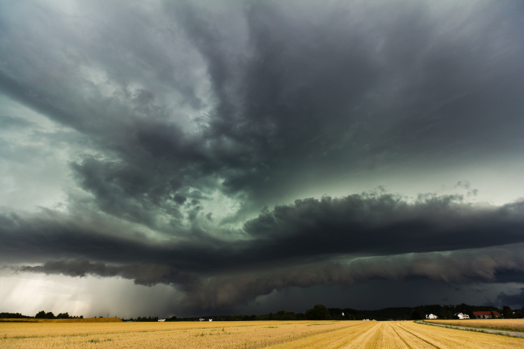 Dunkle Gewitterwolken türmen sich am Himmel. Darunter liegt ein weites Feld.