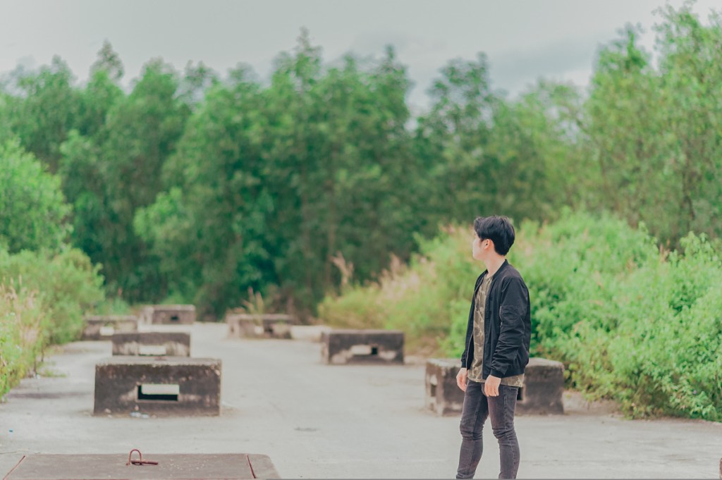 Ein junger Mensch steht auf einer Betonfläche und schaut in Richtung Waldrand.